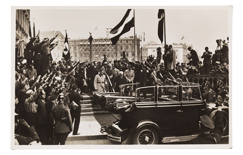 Hindenburg and Hitler are walking down a staircase to an open-top car, surrounded by a crowd of people with outstretched arms. Police officers, photographers and cameramen are in attendance. The northern façade of the Berlin City Palace can be seen to the left; the Kommandantur building on Unter den Linden is visible in the background.
