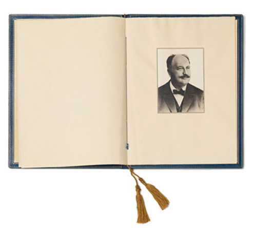 Open book, on the right a portrait photograph of a man with a mustache in a dark suit and bowtie.