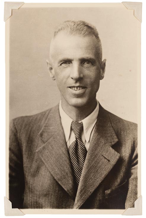 Portrait photo of a gaunt man in a suit smiling at the camera.