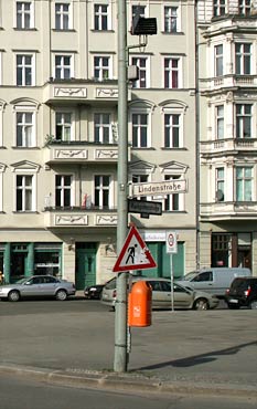 Straßenschild mit Mülleimer und Baustellenschild, im Hintergrund Häuser