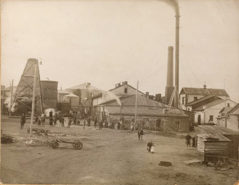 Historical photo of the oil refinery, people, buildings, and vehicles