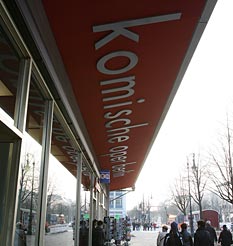 Sign for the Komische Oper seen from below, with passers-by and street view