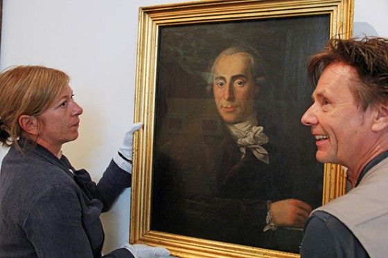 A woman and a man holding a painting against the wall
