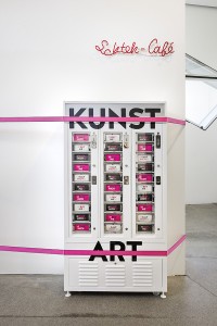 A white vending machine with the inscription "Art", strung up on the wall with pink slackline cables