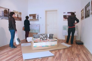 People in a room with photographs on the wall and the pop-up book on the floor