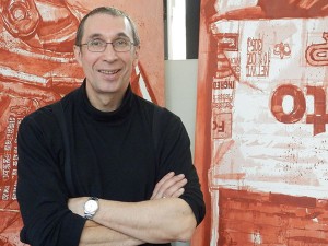 A smiling man in front of red paintings