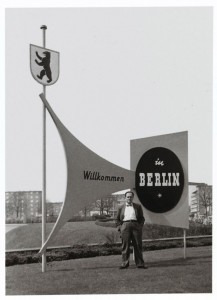 Fred Stein, behind him signs saying "Welcome to Berlin" (in German)