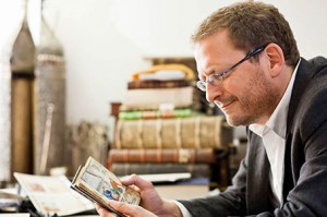 A man sits at a table and holding an open book in his hands