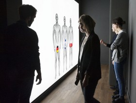 Vistitors in front on the Installation "Personalausweis" with three nacked man. There genitalia are covered with maps of Turkey, Germany and Israel