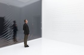 Man in a completly white room with white letters on the wall