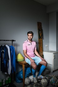 Young man sitting on a table with a lot of soccer balls at his feet