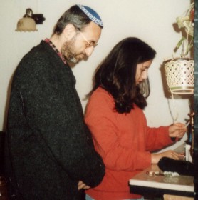 A young woman holding a candle on a candlestick; next to her, a man with a kippah.