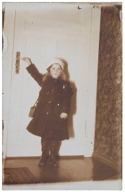 Black and white photograph of a girl standing in front of a door