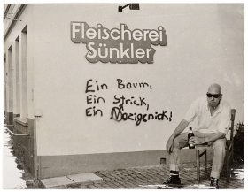 A man with a beer bottle sitting in front of a wall with the instription "Butcher's shop Sünkler"