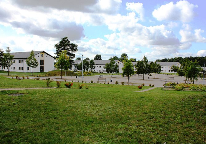 In the foreground large grassy area, in the background trees, cobblestone paths, benches, and cell houses