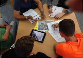 Young people around a table look at texts and a tablet