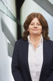 Portrait of a woman standing in a big open staircase. She wears a dark-blue blazer and a white blouse mit dunkelblauem Blazer und weißer Bluse, die in einem großen, offenen Treppenhaus steht