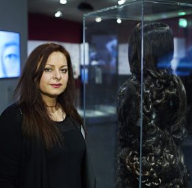 Woman standing next to a showcase in which there is a sculpture made of hair