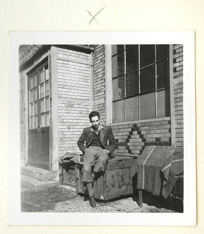 A young man sits in front of a house (black and white photo)