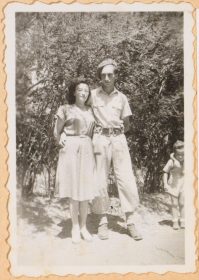 On the black and white picture Walter Frankenstein holds his wife Leonie in his arms. He wears a military uniform, Leonie a summer dress. They do not smile. Bushes grow in the background..