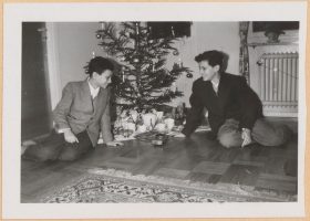 In the black-and-white photo, the two boys are sitting in front of a Christmas tree, smiling at the gifts that are strewn beneath it.