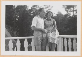In the black-and-white photo, Leonie is sitting in a summer dress on the rail of a balcony. Walter stands next to her with his left arm around her and holding a cigarette in his right hand.