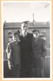 Rolf Rothschild stands in the middle of the black-and-white photo with his arms around the two boys. All three are wearing suits.