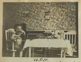 Black-and-white photography of a laughing toddler sitting on a chair next to a birthday table.