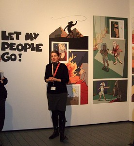 Eine junge Frau vor einem Comic an der Wand mit der Aufschrift »Let my people go!«