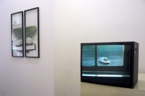 Ausstellungsansicht, links Glasrahmen, rechts Fernseher mit Bild vom Meer