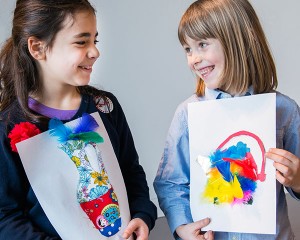 Zwei Mädchen zeigen sich lächelnd ihre Entwürfe einer Vase und einer Teekanne.