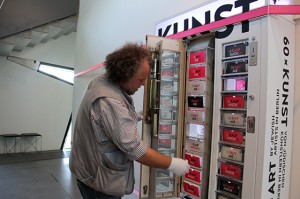 Ein Mann mit weißen Handschuhen zieht an einem Fach des Kunstautomaten