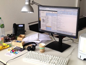 Ein Schreibtisch mit PC Bildschrim, Tastatur, Büchern und einer Kaffeetasse
