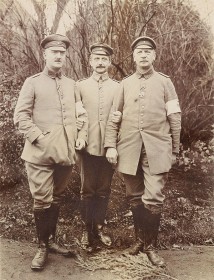 schwarz-weiß Fotogfrafie mit drei uniformierte Sodaten frontal und stehend vor einer Grünanlage