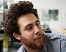 Portätfotografie eines jungen Mannes mit Bart und lockigem Haar, nach rechts blickend