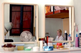 Farbfotografie mit zwei Spiegeln an einer Wand und Spiegelung einer sitzenden alten Frau