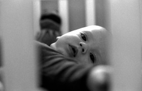 Schwarz-weiß Fotografie mit einem Kleinkind in einem Gitterbett