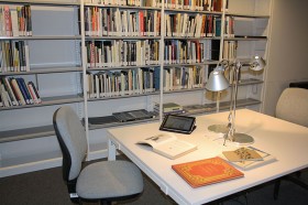 Tisch mit Büchern und Tablet, im Hintergrund Bücherregale