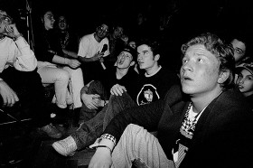 Schwarz-weiß Foto: Jugendliche sitzen auf dem Boden und auf Stühlen