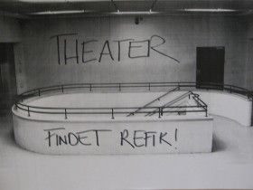 Ein graues Treppenhaus an dessen Wand der Satz "Theater. Findet Refik" angesprüht ist
