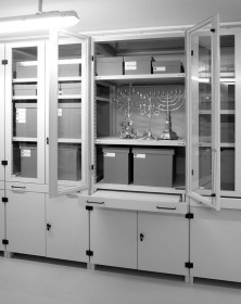 Fotografie mit Ansicht eines geöffneten Glasschranks mit Sicht auf grauen Kartons und drei Leuchter