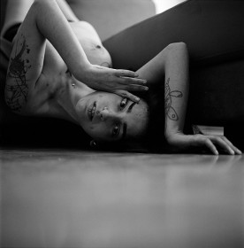 Schwarz-weiß Fotografie iener jungen Frau, die mit nacktem Oberkörper auf dem Boden liegt