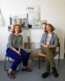 Ein Zwillingspaar auf Stühlen sitzend vor Bildern an der Wand