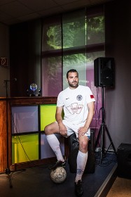 Junger Mann in Sportkleidung mit Fußball vor einer Bar