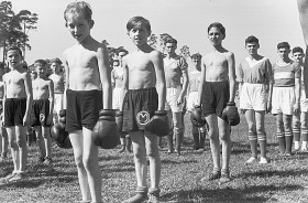 Jungen mit nackten Oberkörpern stehen in Reihen auf einem Sportfeld