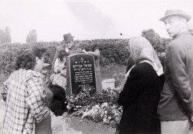 Schwarz-Weiß-Fotografie von Menschen an einem Grab mit Blumen