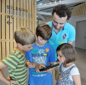 David Studniberg schaut mit zwei Jungen und einem Mädchen auf ein iPad