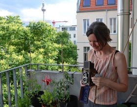 Birgit Glatzel steht mit ihrer Rolleiflex-Kamera auf ihrem Balkon