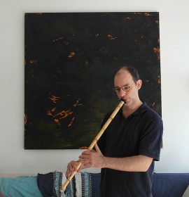 David Benforado mit einer Nay-Flöte vor einem abstrakten Gemälde