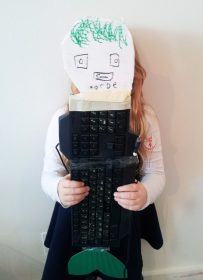 Kind hält gebastelte Fantasiefigur aus einer Tastatur mit Schwanzflosse und Papiergesicht vor sich